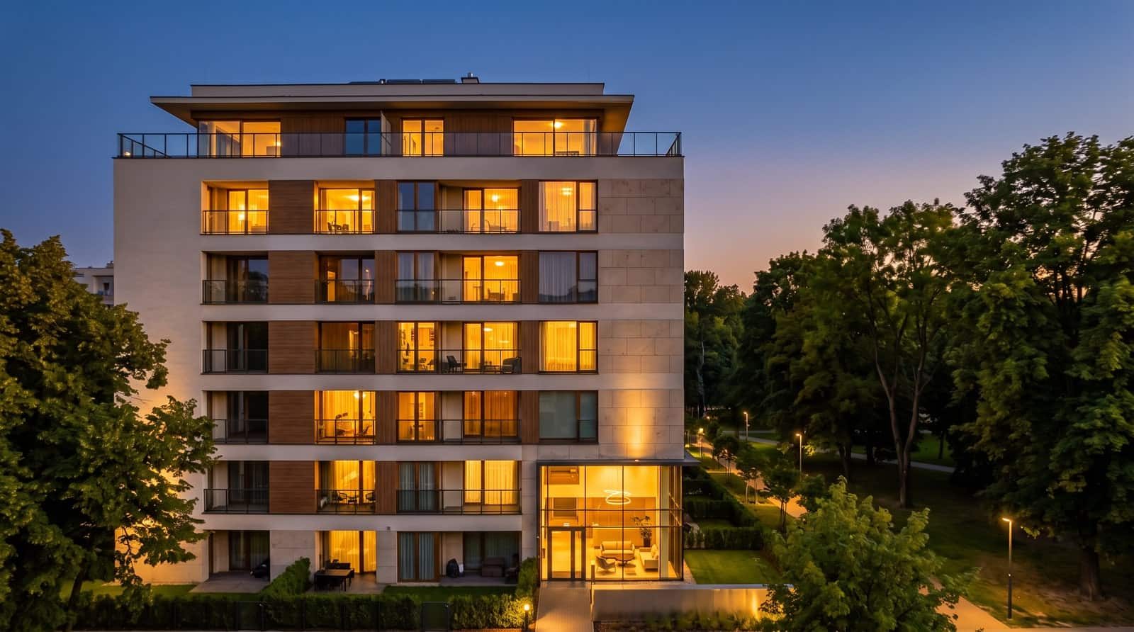 A residential building at dusk with the windows of every apartment lit from within.
